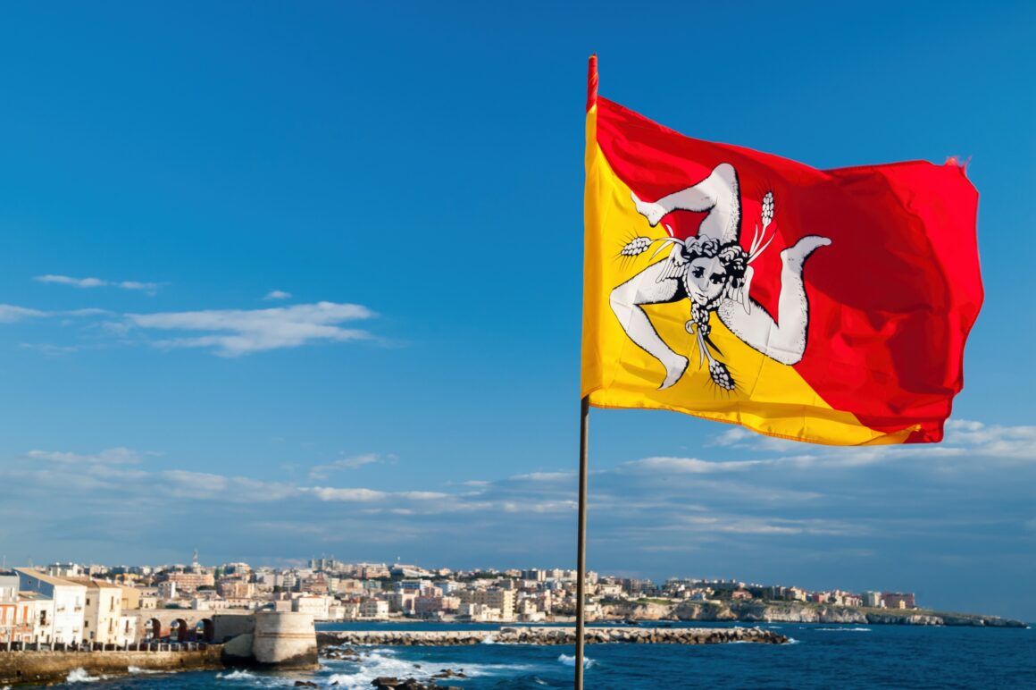 Die wehende Flagge Siziliens an der Strandpromenade von Syrakus mit Blick auf die Stadt.