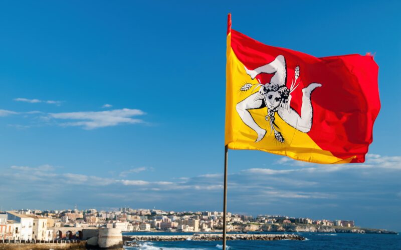 Die wehende Flagge Siziliens an der Strandpromenade von Syrakus mit Blick auf die Stadt.